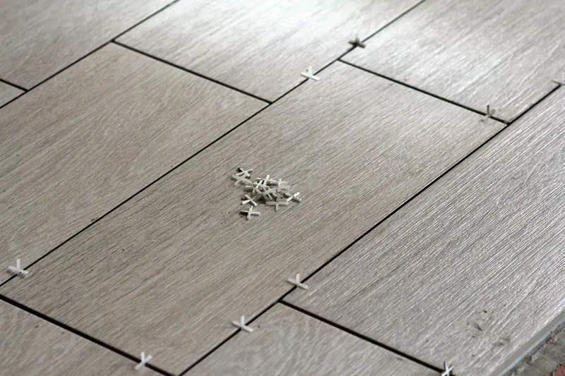 Porcelanato cinza em assentamento, com espaçadores plásticos brancos entre as peças
