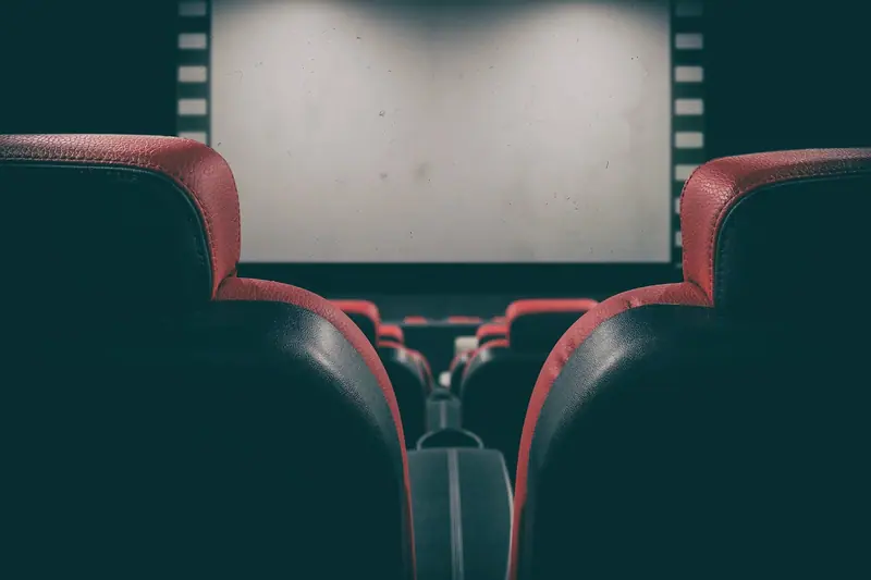Encostos de poltronas de cinema vistos por trás, voltados para uma tela clara