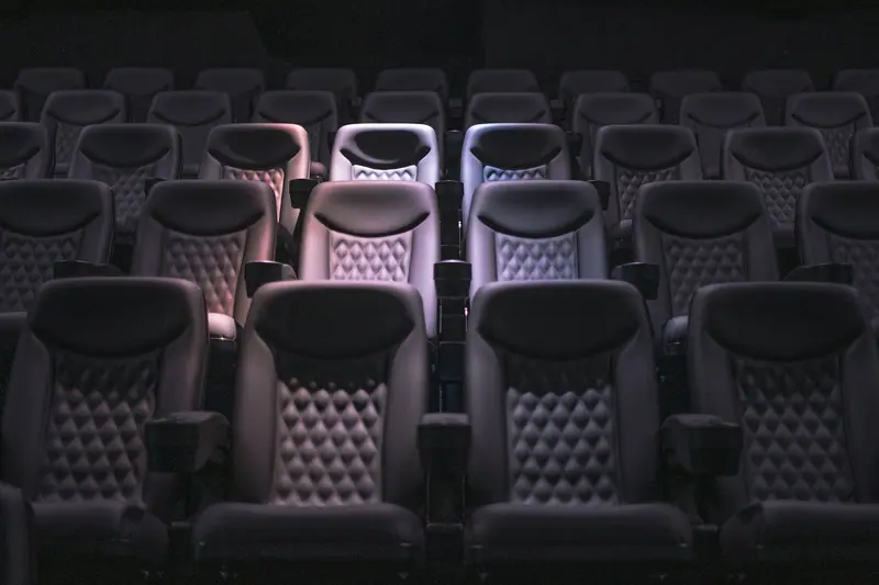 Fileiras de poltronas reclináveis estofadas numa sala de cinema com pouca luz