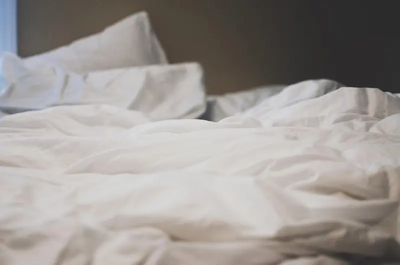 Lençóis brancos amarrotados numa cama desfeita, em luz suave