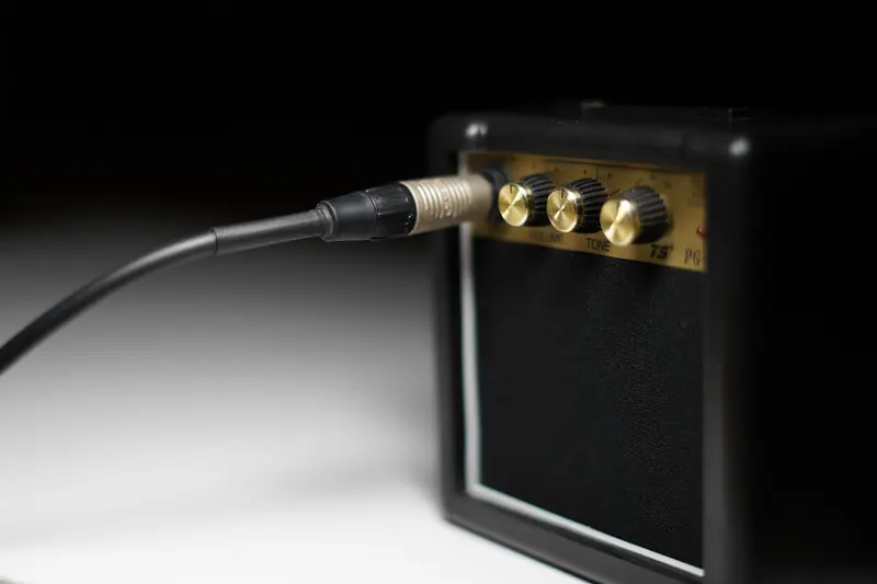 Amplificador pequeno de guitarra com o cabo conectado, sobre uma superfície branca