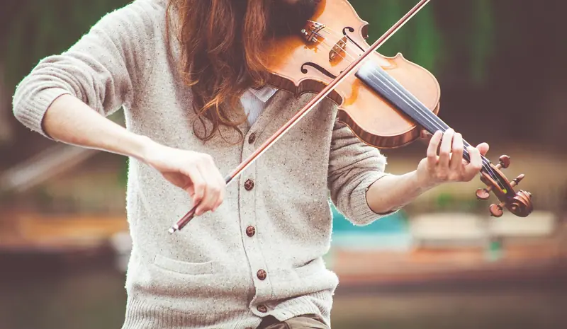 Pessoa de cardigã claro tocando violino, vista do pescoço para baixo
