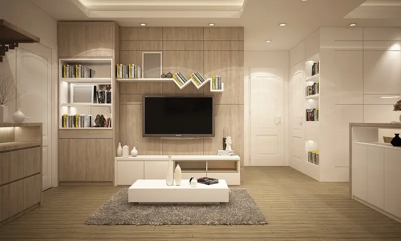 Sala com televisão na parede, estante clara e uma porta branca ao lado