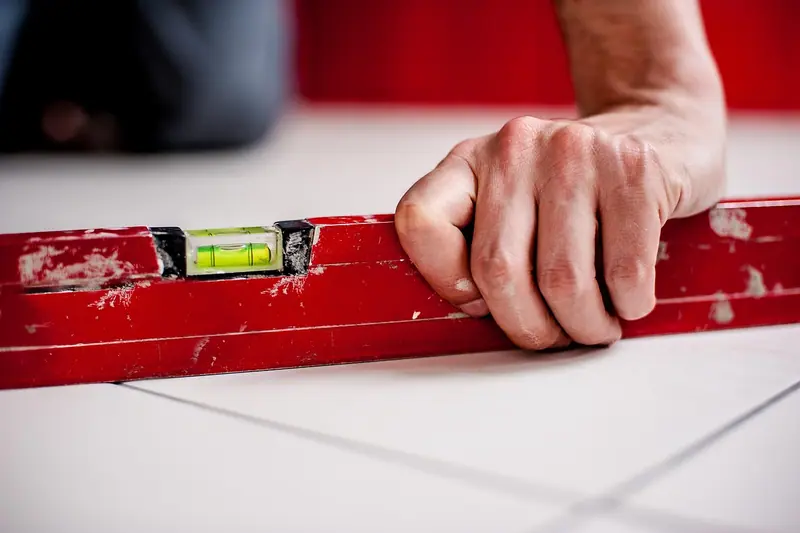 Mão segurando um nível de bolha vermelho apoiado sobre um piso claro