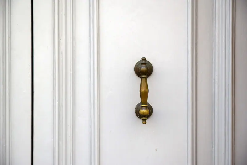 Detalhe de uma porta branca de painéis com puxador dourado