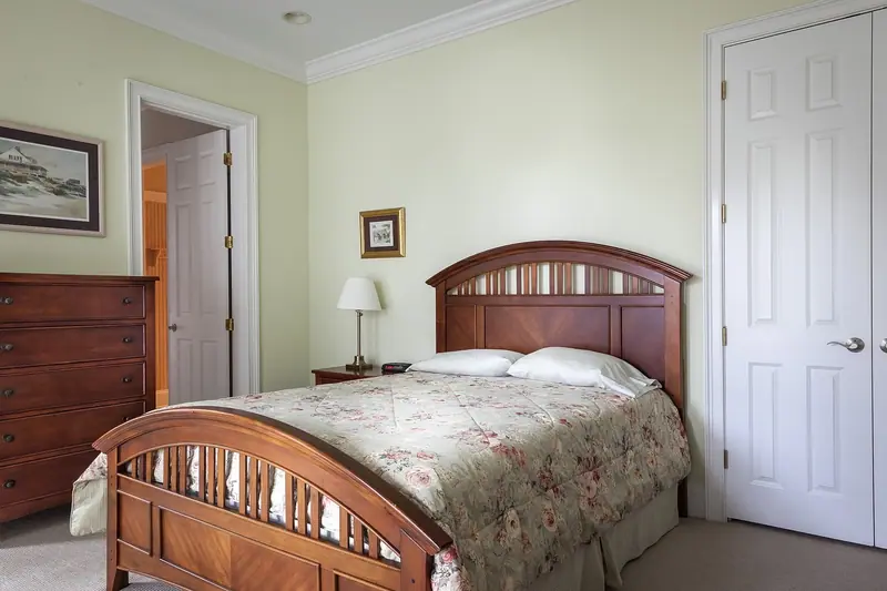 Quarto com cama de madeira, cômoda e porta branca de painéis aberta ao lado