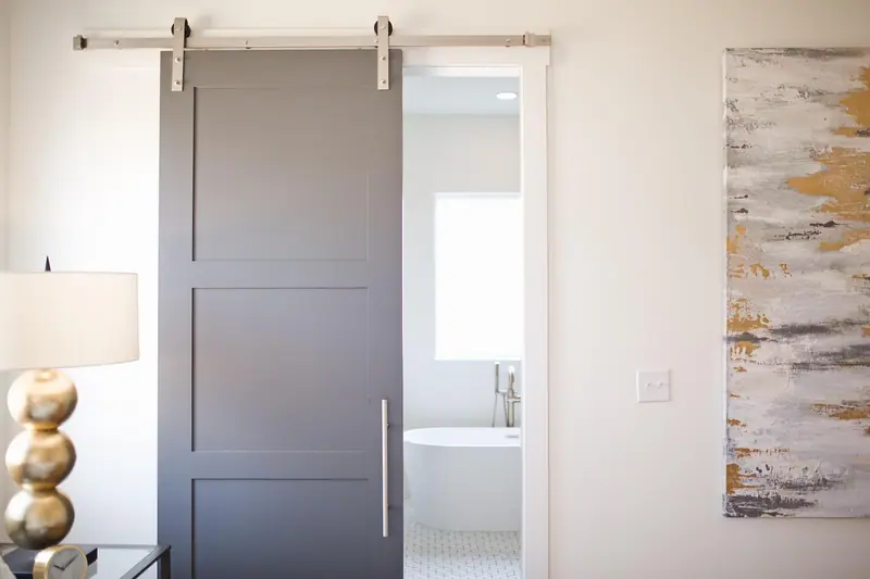 Porta cinza de correr no estilo celeiro, com trilho aparente no alto, aberta para um banheiro