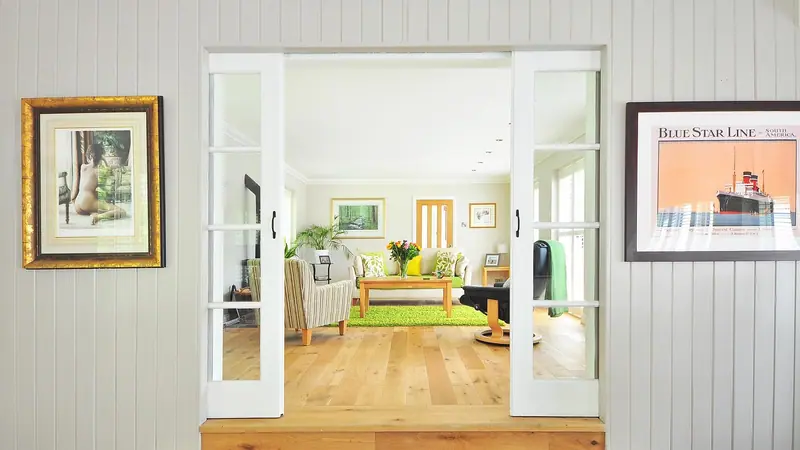 Porta de correr branca com vidros, aberta entre um corredor e uma sala clara com piso de madeira