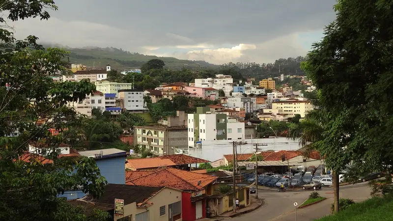 Bairro de casas e pequenos prédios num morro, com ruas, carros estacionados e árvores