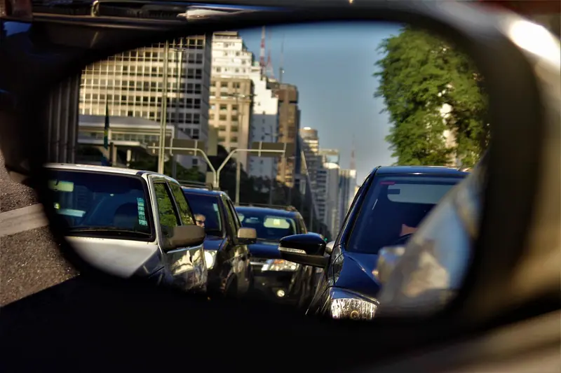 Retrovisor de carro refletindo uma avenida com carros parados e prédios ao fundo