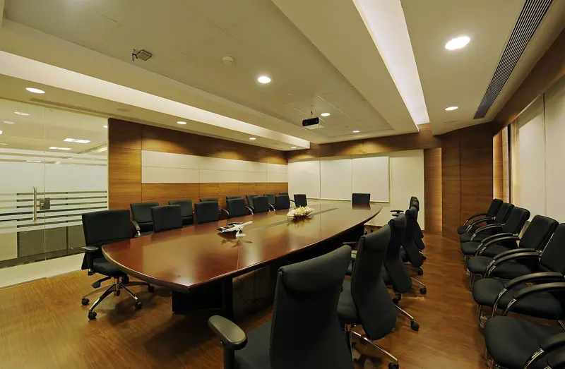 Sala de reunião com mesa comprida, cadeiras pretas e divisória de vidro com faixa jateada à esquerda