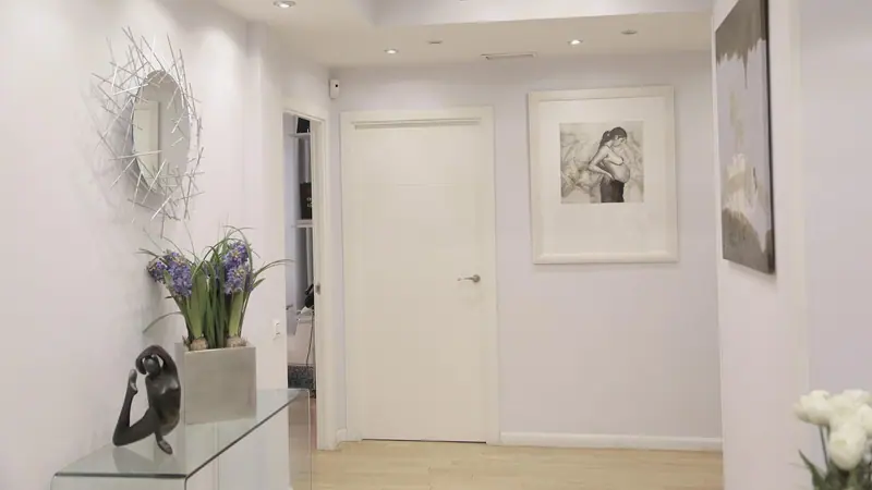 Hall claro com piso branco, quadros na parede e uma porta branca fechada ao fundo