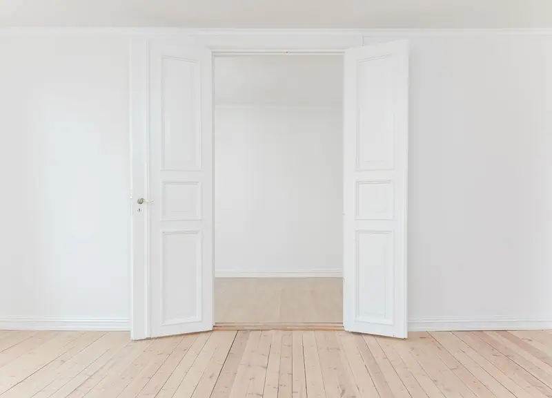 Porta branca de duas folhas aberta para um cômodo vazio com piso de madeira clara