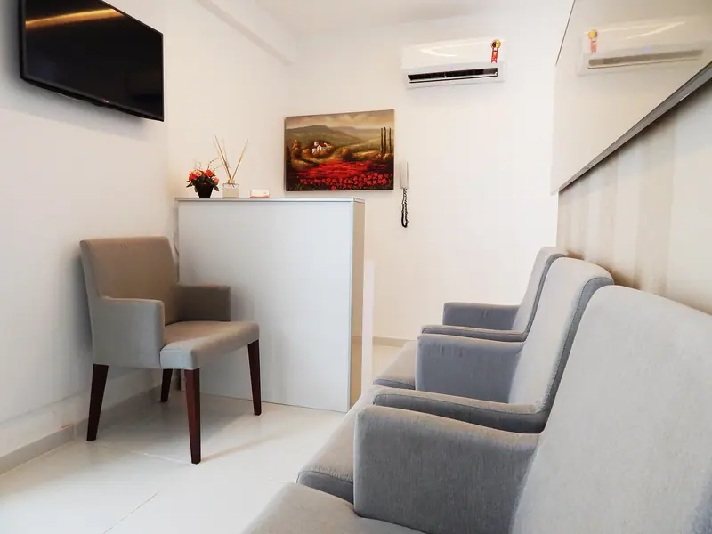 Sala de espera clara com poltronas cinza, balcão branco e quadro na parede