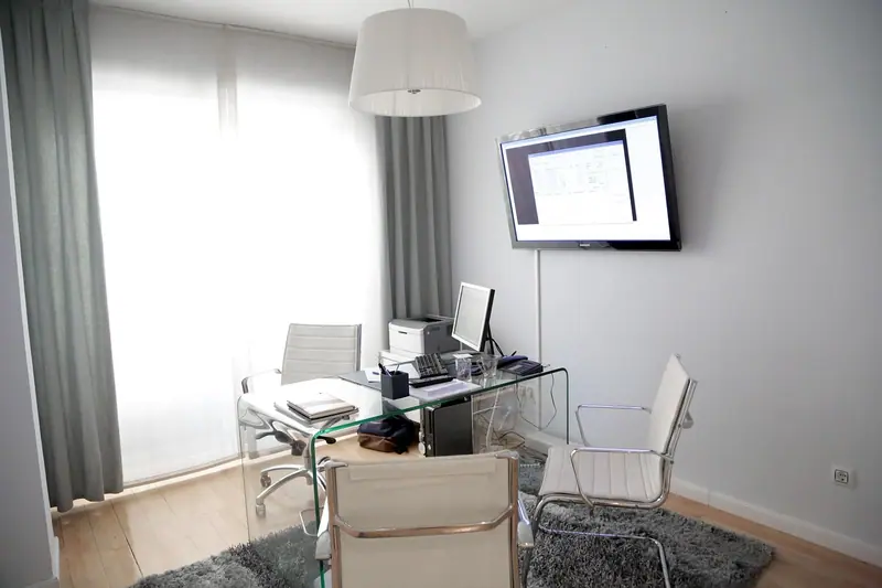 Sala de atendimento clara com mesa de vidro, cadeiras brancas, tapete e cortinas