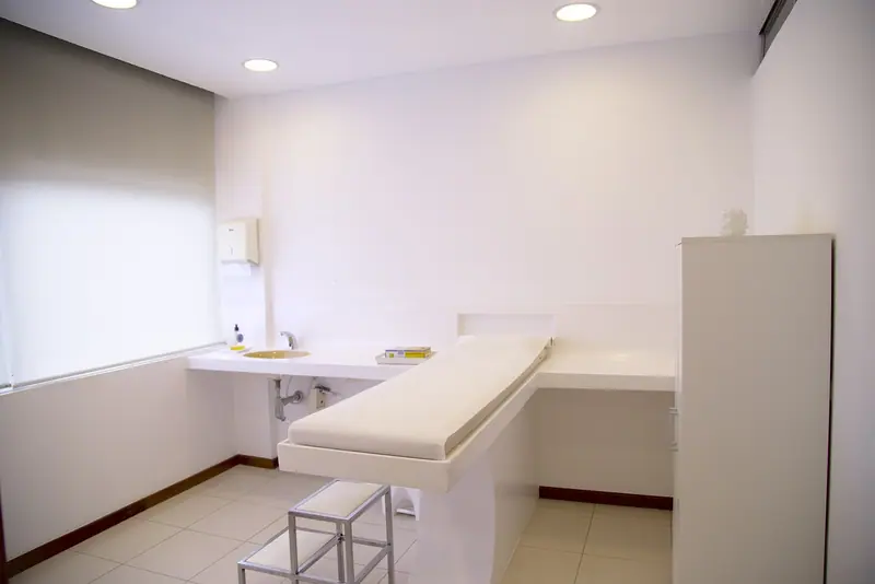 Consultório claro com maca, pia e armário branco, sem pessoas