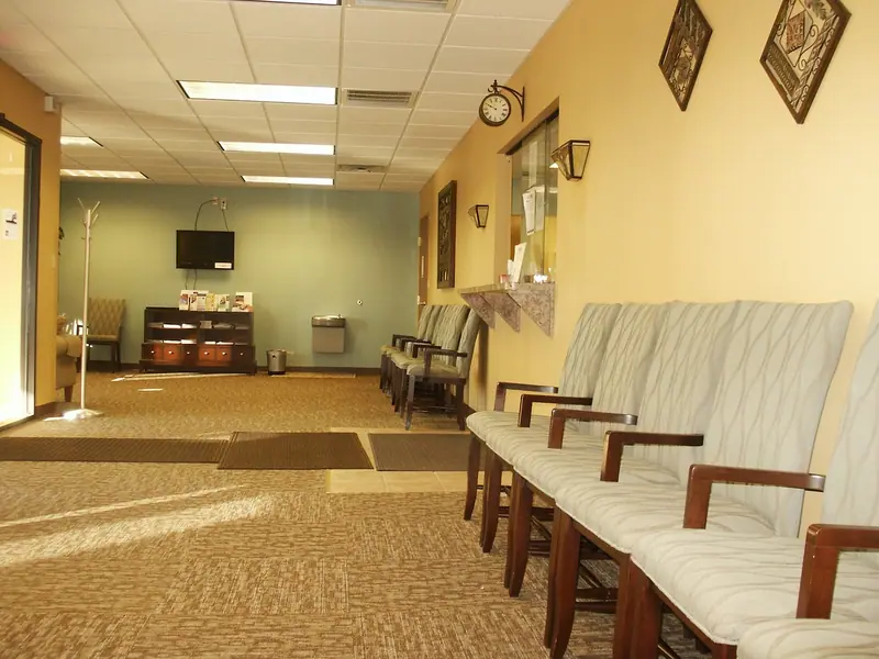 Sala de espera com poltronas claras enfileiradas junto à parede e carpete no chão