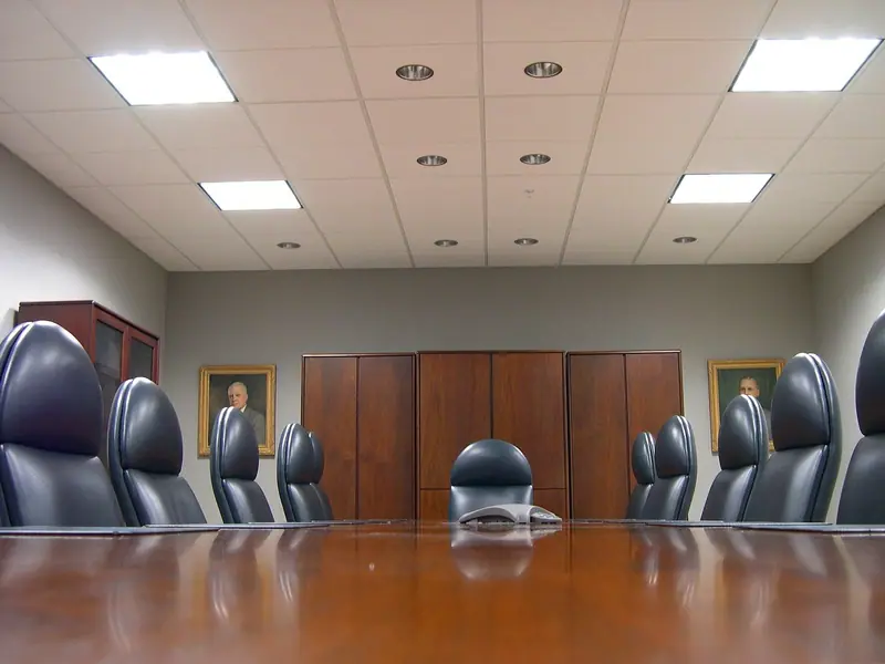 Sala de reunião com mesa longa de madeira e cadeiras de couro, armários ao fundo