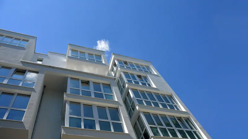 Prédio residencial branco com várias janelas salientes, visto de baixo contra o céu azul