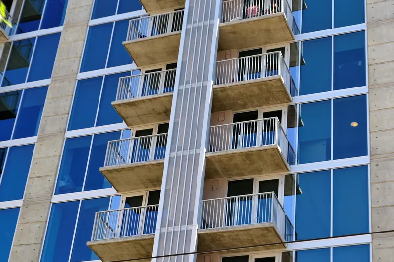 Prédio moderno com varandas de grade e grandes painéis de vidro azulado na fachada