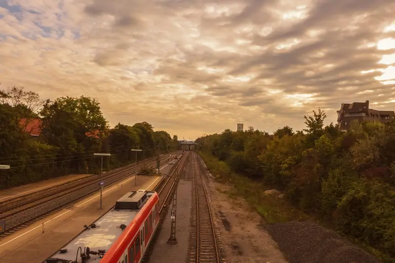 Trem passando por uma linha a céu aberto entre árvores, visto do alto, com o céu do fim de tarde