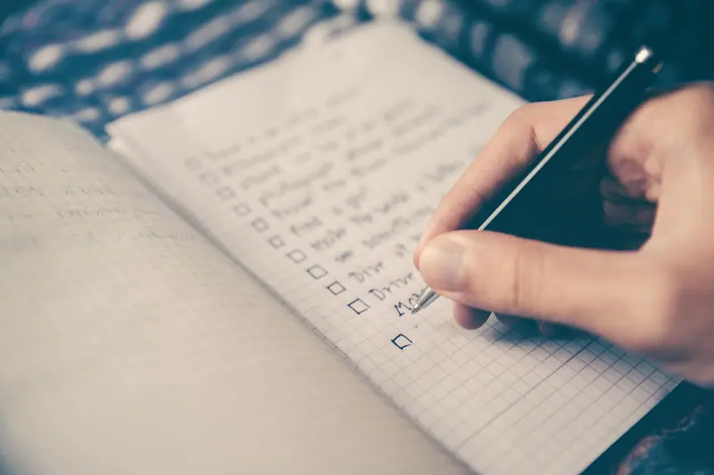 Mão escrevendo uma lista de tarefas num caderno quadriculado