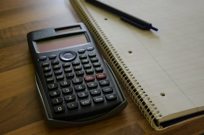 Calculadora preta sobre uma mesa de madeira, ao lado de um caderno de espiral e uma caneta