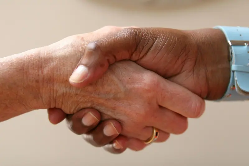 Aperto de mãos entre duas pessoas, em close, sobre um fundo claro
