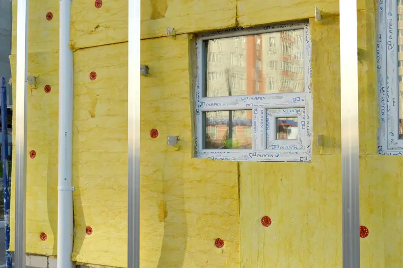 Caixilho branco de janela recém-colocado numa parede em obra, cercada por placas de isolamento amarelas