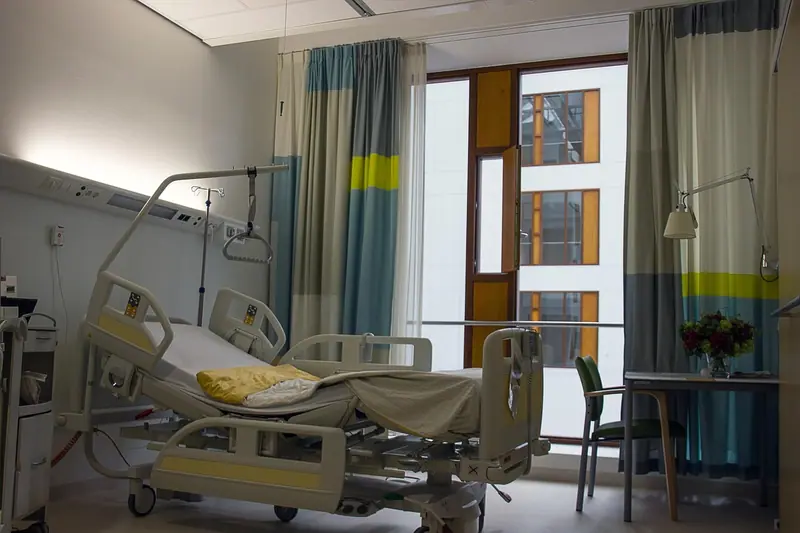 Quarto de hospital com cama hospitalar, cortinas coloridas e janela ampla