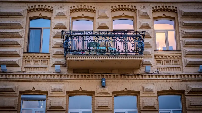 Fachada clássica de prédio com ornamentos, janelas altas e uma sacada de ferro trabalhado