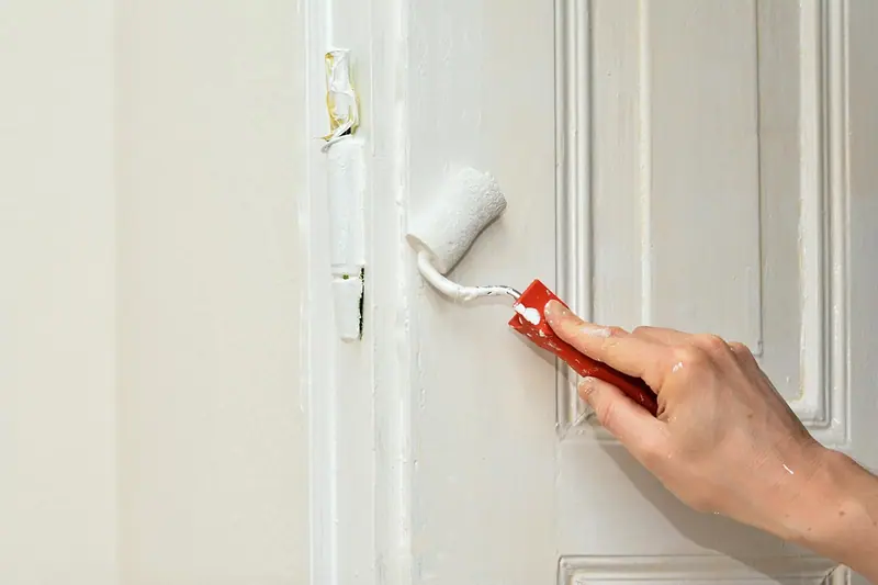 Mão pintando uma porta branca com um rolo pequeno