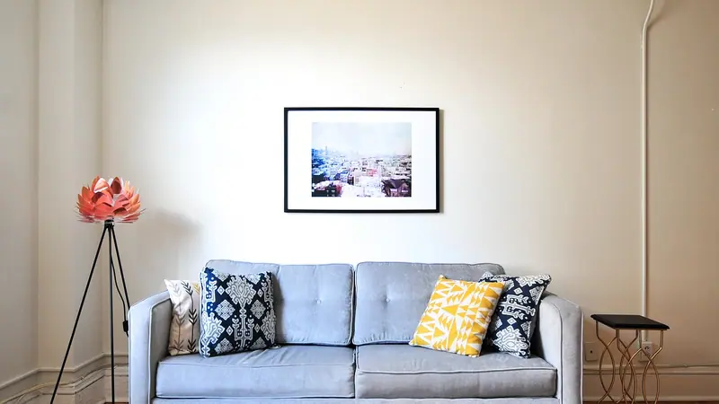 Sala com sofá cinza e almofadas estampadas, quadro na parede e piso de taco em espinha de peixe