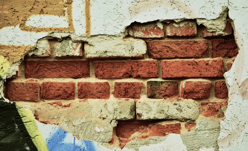 Parede com o reboco quebrado, deixando os tijolos à mostra