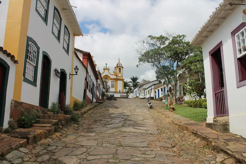 Rua de pedras irregulares em cidade histórica, com casas brancas e uma igreja ao fundo