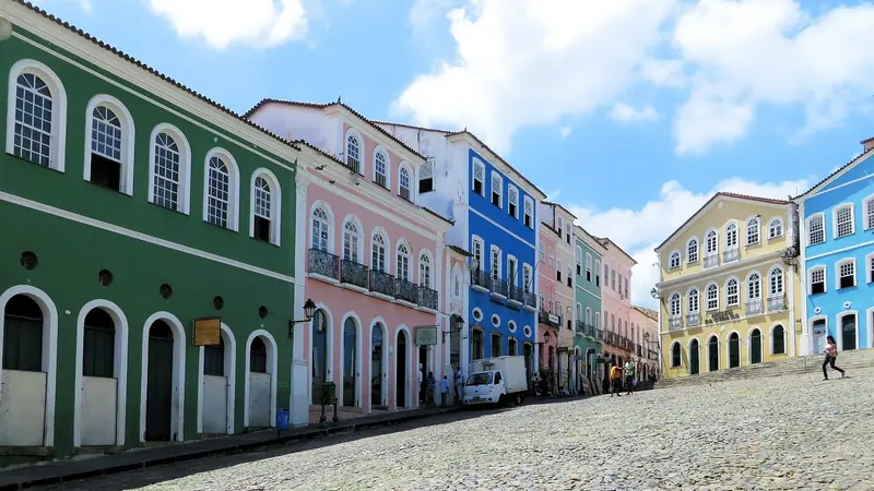 Rua larga de pedras com casarões coloridos dos dois lados, sob um céu azul com nuvens