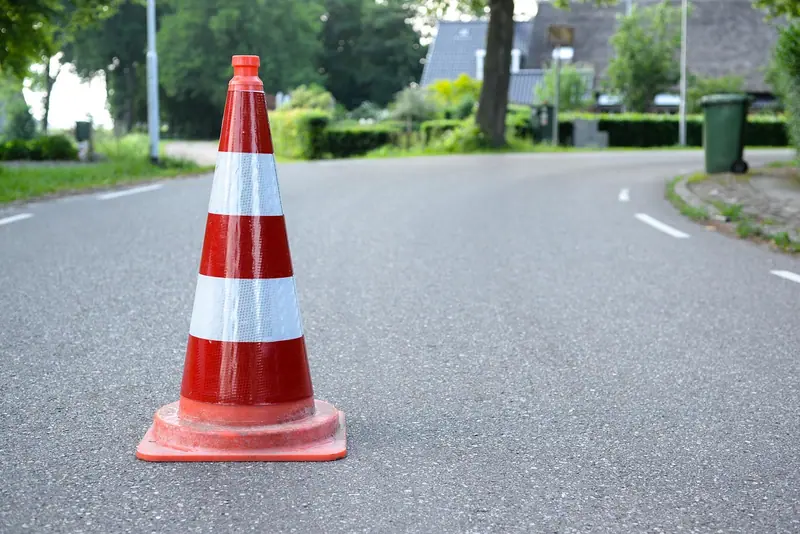 Cone de trânsito laranja e branco no meio de uma rua residencial, com casas e árvores ao fundo