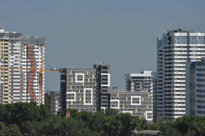 Torres residenciais altas e recém-construídas ao lado de prédios menores e de uma faixa de árvores