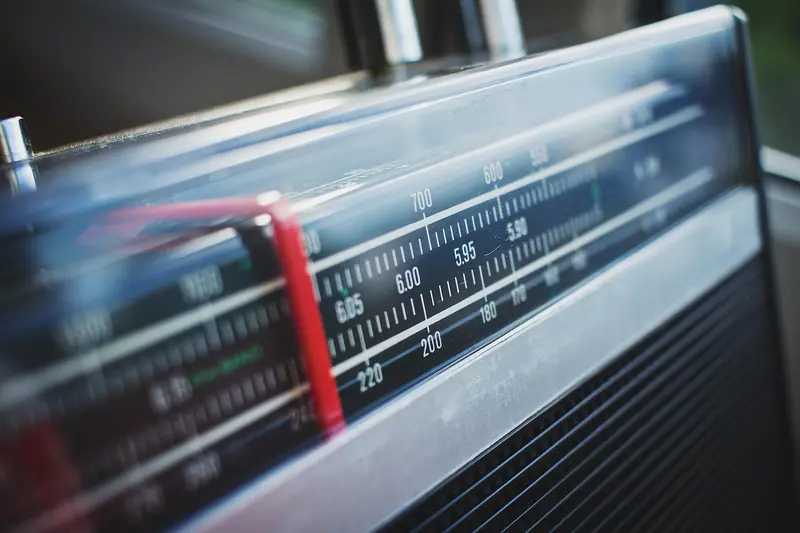 Detalhe do mostrador de frequências de um rádio antigo, com números e ponteiro vermelho
