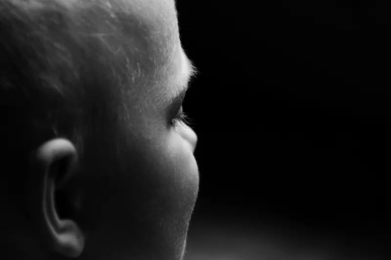 Foto em preto e branco do perfil de uma cabeça na penumbra, com a orelha iluminada