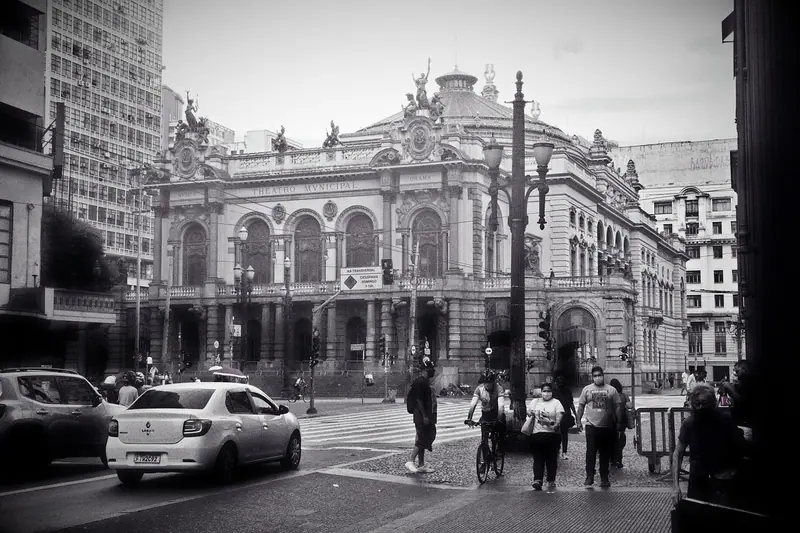 Foto em preto e branco de uma rua do centro de São Paulo com carros e pedestres diante do Theatro Municipal