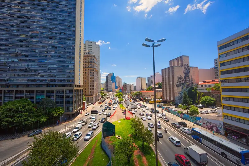 Avenida larga de São Paulo com várias faixas de carros e ônibus, entre prédios altos