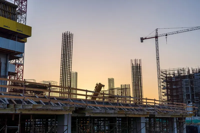 Obra de prédio com pilares de concreto, ferragens à mostra e guindaste ao fundo no fim de tarde