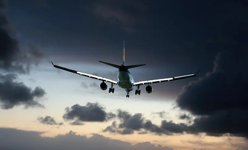 Avião com o trem de pouso baixado contra um céu escuro de fim de tarde