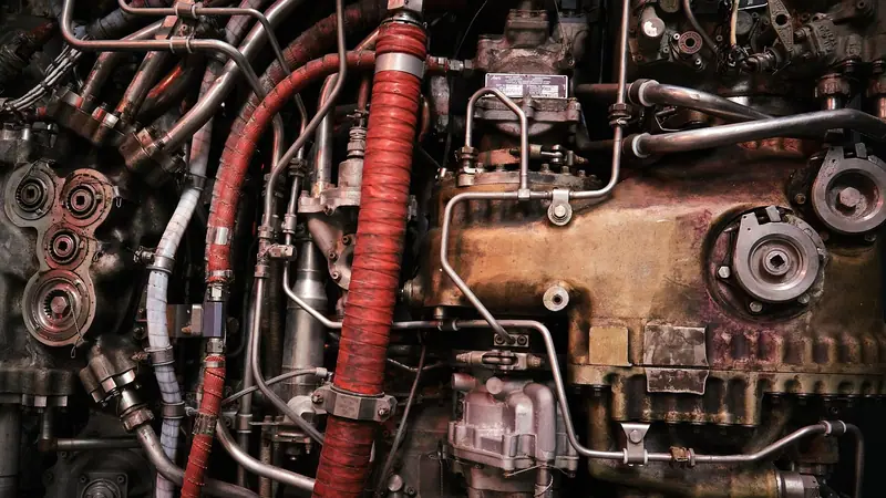 Detalhe de um motor industrial com tubulações, mangueiras vermelhas e peças metálicas
