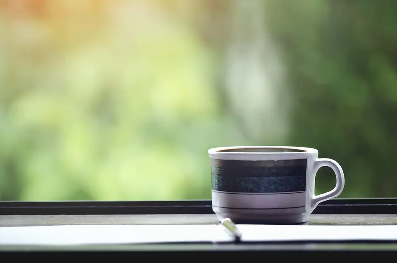 Xícara de café no parapeito de uma janela, com folhagem verde desfocada ao fundo