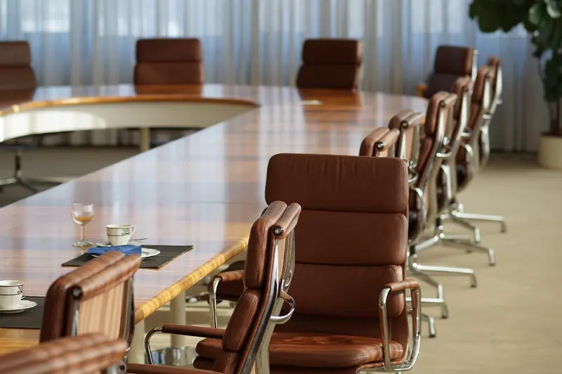 Mesa de reunião de madeira encerada com cadeiras de couro marrom ao redor, numa sala clara