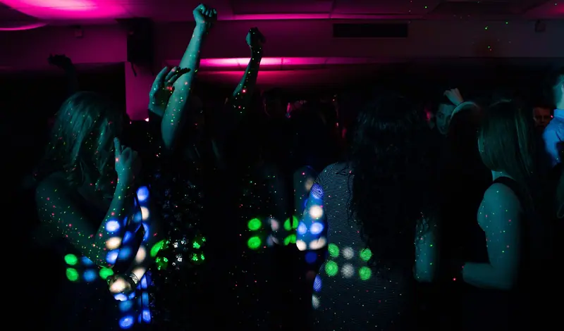 Pessoas dançando numa festa à noite, desfocadas, sob luzes coloridas