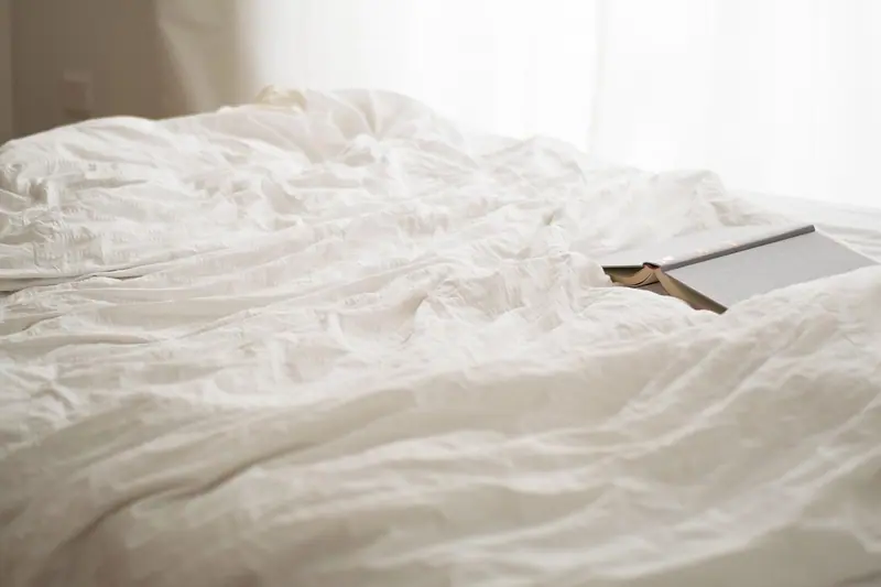 Cama com lençóis brancos amassados e um livro aberto sobre o edredom