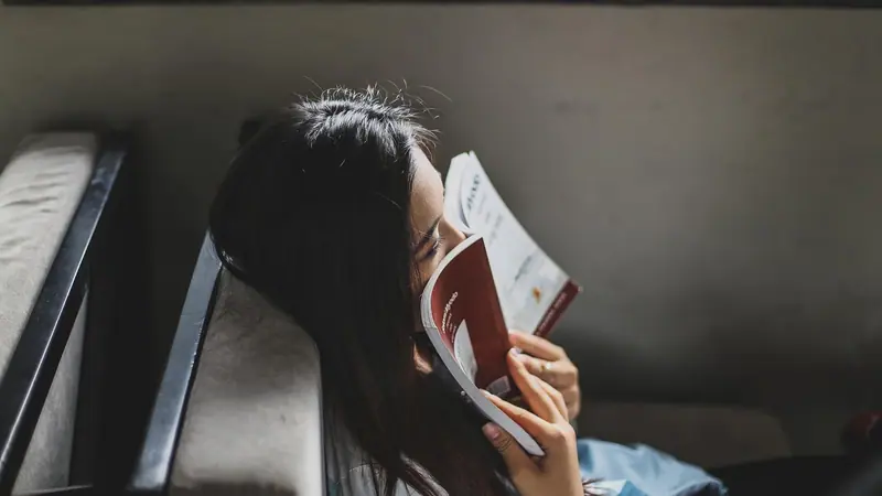 Mulher deitada num banco com um livro aberto cobrindo o rosto